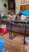 Side view of one TV tray showing black resin top and black adjustable metal legs in U-shaped frame.