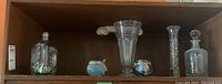 Shelf containing 3 apothecary bottles (one with a cork stopper), tall fluted clear glass vase, 2 small navy blue ceramic pots, and 1 glass candle holder.