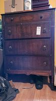 Front view of the vintage wooden dresser showing four drawers, unique metal pulls on bottom three drawers, and carved wood details.