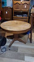 Photo showing the full round wooden table with a worn finish, placed on a wood floor basement setting.