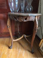 Full view of the carved wooden side table showing the carved cabriole legs, apron with lattice and leaf pattern, and clear glass vases on top.