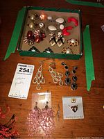 Lot of assorted costume jewellery earrings displayed in a box and on a wooden surface, showing variety of styles, colors, and materials.