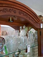 Crystal pitcher, ice bucket, decanter, and glasses displayed on a glass shelf in wooden cabinet