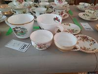 Overview of cups, mugs, and saucers from various brands showing floral patterns and gold trim on white porcelain.