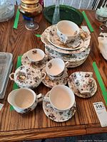 Full set overview with plates stacked and cups, creamer, sugar bowl arranged on table showing fruit decorative pattern.
