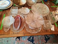 Various glass serving plates, pedestal stand plate, bowls, glass dishes, and tinted oval plate packed together on table.