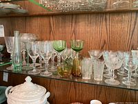 Shelf with assorted glass stemware including patterned clear, green tinted, and plain glasses of various shapes and sizes.