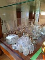 Full view of the Bohemia glassware set including sherry glasses, pitcher, ashtray, salt and pepper shakers, and napkin holder on a shelf.