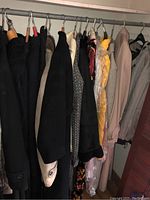 View of assorted ladies coats and jackets hanging on rack in closet, showing multiple styles, colors and materials.