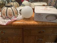 Three ceiling light fixtures on a wooden dresser, including Tiffany style fixture, white globe, and boxed flush mount light