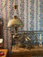 Photo showing two brass swag pendant light fixtures with chains and domed shades, hanging uninstalled inside a room with floral wallpaper background.