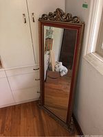 Full view of the tall ornate framed mirror leaning against a kitchen cabinet, showing the mirror's size and frame design.