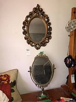 Photo of two oval mirrors, one mounted on wall with ornate frame and one on stand on surface below.