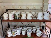 Two shelves filled with assorted bone china and porcelain mugs decorated with floral patterns and colorful designs.