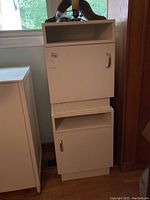 Pair of white melamine night tables stacked on each other near a window, showing overall condition and size.