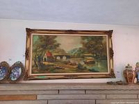 Full view of the framed landscape painting depicting a river scene with a house, stone bridge, boats, and trees.