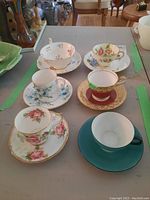 Top-down view showing all six cups and saucers, with varied floral and color patterns including blue, red, and pink accents