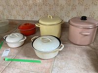 Five utility pots on countertop: two Waterford Colorcast pots, orange-red Le Creuset pot, two white enamel pots.