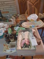 Overview of multiple items on table including ceramic vase in box, brass vase, candlesticks, animal figures and more