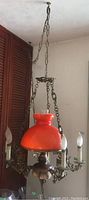 Metal and ceramic ceiling light fixture with orange glass shade and metal shade holder, four candle-style bulbs, and hanging link chain attached to ceiling.