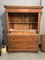 Front view of antique solid wood hutch showing three drawers with ring handles, open shelving with two small drawers, and two detached wooden doors leaning beside it.