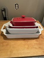 Four stoneware baking dishes stacked together, two white and two red dishes, one red dish includes a lid with a knob.