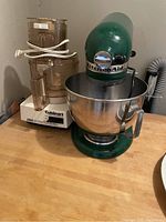 Photo showing older Cuisinart food processor and green KitchenAid stand mixer side by side on wood countertop.