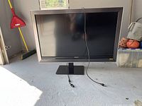 Sony Bravia 52-inch TV with adjustable stand placed on a concrete floor. Power cord is visible on front of the TV.