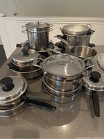 Photo showing assorted stainless steel cookware including pots, pans, steamer insert, and colander.