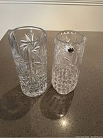 Two tall crystal vases standing side by side on a countertop, showing detailed cut patterns on clear crystal.