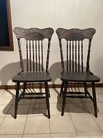 Two Victorian farmhouse-style wooden dining chairs side by side, both showing detailed carved top rails and spindle backs.