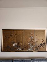 Full view of three framed Asian art panels mounted side-by-side on a wall, showing gold backgrounds with floral motifs.