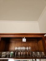 Wide shot of bar cabinet shelf with groups of glasses including stemmed wine glasses and short Perrier water glasses.