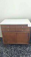 Front view of the Town Set wood cabinet showing white top, four drawers with metal knobs, and sliding door compartment below.