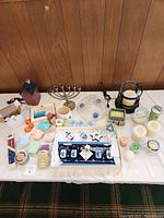 Photo showing the entire lot arranged on a white cloth including the brass menorah, ceramic potpourri burners, various white candles, packaged small candles, Chanukah serving dish with dreidels, and other small candle-related accessories.