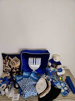 Wide shot of all included items in the lot, showing two decorated pillows, kippahs, teddy bear, menorah, stockings, and paper supplies spread on a surface.