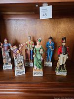 Front view of six figurine liquor bottles displayed on wooden shelf showing detailed characters.