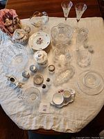 Overview of all crystal bowls, glassware, china plates, teapot, and floral music box on table.