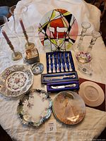Full overview of lot items on white cloth, includes clock, plates, cutlery set, candle holders