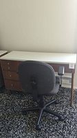 Desk and rolling chair side view showing desk drawers and chair backrest.