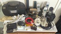 Full view of the lot showing Venturer CD/tape player, multiple cordless phones, extension cords, power strips, adapters, flashlights, camera, and assorted cords