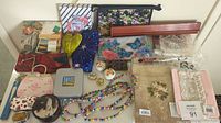 Vintage accessories and collectibles displayed on table, including picture album, small boxes, wallets, sachets, fan, and bags.