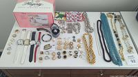 Wide shot of all the jewelry items including watches, rings, necklaces, earrings, and jewelry cleaner box on a dresser.