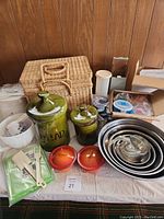 Overview of kitchen and picnic items on table: ceramic canisters, picnic basket, rice cooker, stainless bowls, utensils, containers