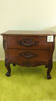 Front angled view of wood nightstand showing two carved drawer fronts and claw feet base.