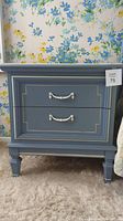 Front view of blue Dixie nightstand with two drawers, white decorative handles, and decorative molding on drawer fronts.