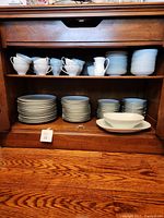 Full china set shown inside wooden cabinet, includes cups, saucers, plates, bowls, and a pitcher.