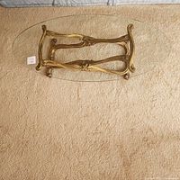 Overhead view showing oval glass top and the gold ornate leg base under it on carpet.