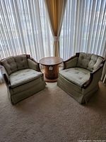 Overview photo showing two silk upholstered Oxford chairs and one round wood table placed in front of a window with curtains.