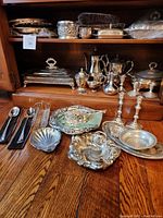 Group of assorted silver serving pieces and tea set arranged on floor and shelf